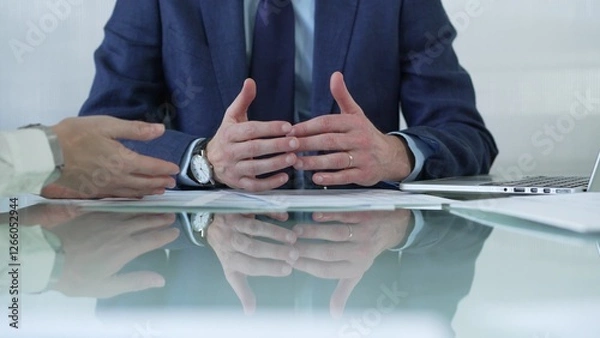 Fototapeta Business partners or lawyers dressed in blue are reviewing and discussing contract papers during a meeting, using a laptop and documents on a glass table. Businesspeople