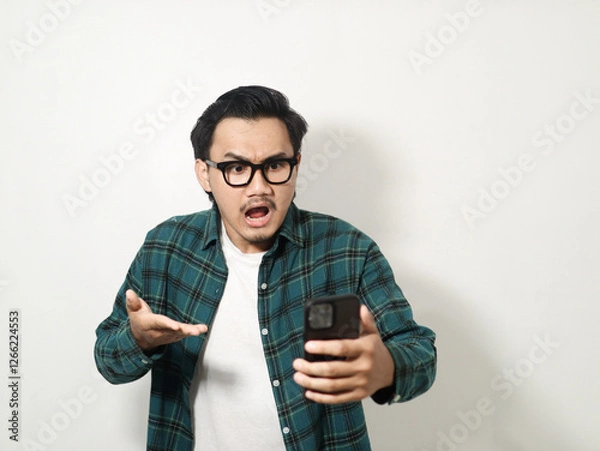 Obraz A man shows an angry expression while looking at his cell phone isolated on white background