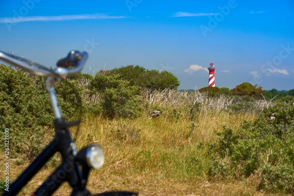 Fototapeta Dutch lighthouse on the horizon. Handlebar of bicycle out of focus. Landscape shot on a sunny bright vacation afternoon. Blue sky for copy space. Holland, Zeeland, Haamstede.