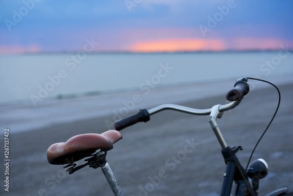 Fototapeta Part from a ladies bike. Handlebar and saddle from a vehicle. Sea landscape at sunrise in Holland.