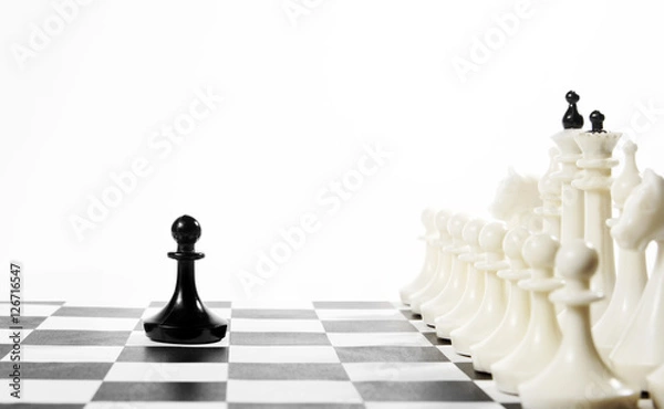 Fototapeta Lonely black pawn in front of enemy team. Courage and boldness. Concept with chess pieces against white background