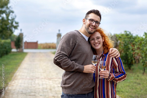 Fototapeta Young couple with glass of vine in hands hug and smile in vineyard