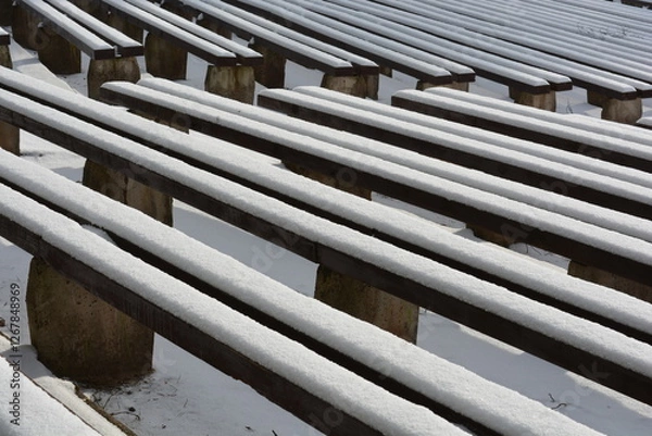 Fototapeta Wooden benches in a winter snowy park, covered with snow. Lines and diagonal 