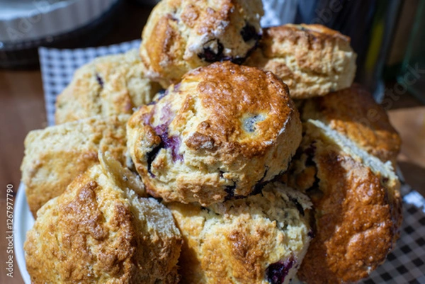 Fototapeta A stack of blueberry scones on a white cake stand. The scones are golden brown and look delicious