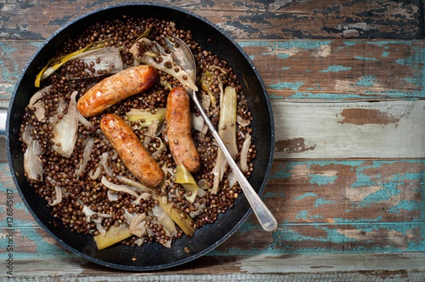 Obraz Sausages cooked with lentils, fennel and fresh leeks in a one pot casserole. Served on a rustic wooden table.