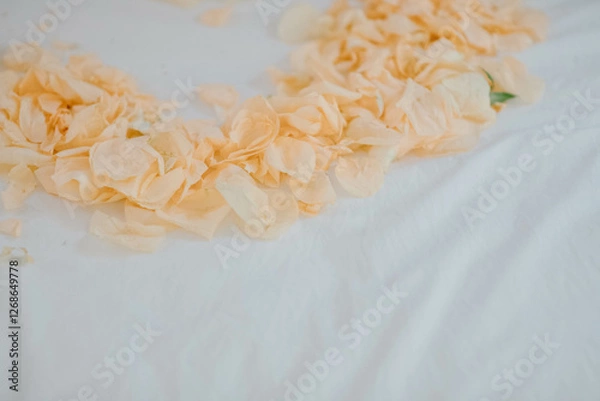 Fototapeta Orange rose petals placed in the shape of a heart on a white bed for newlyweds and brides