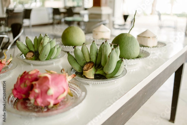 Fototapeta Fruits, including dragon fruit, banana, pomelo, and coconut, placed on a plate on a white wooden table