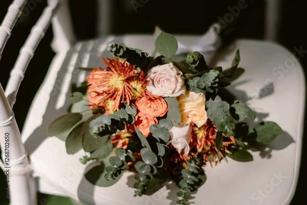 Fototapeta A flower bouquet composed of white, pink, and orange roses, placed on a white chair, with light and shadows