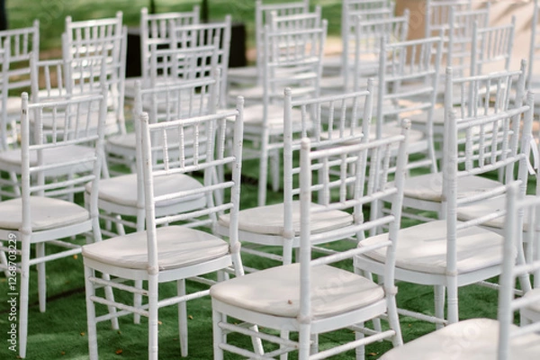 Fototapeta Many white chairs are neatly arranged in an orderly manner to be used in a wedding ceremony held on the grassy field in the garden