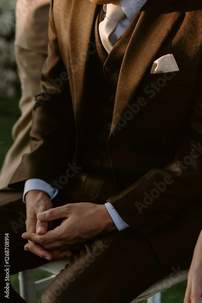 Fototapeta Groom in wedding suit with long sleeves. Handsome man in tux. Close up. Dark brown suit and cream tie. There was morning light falling on him