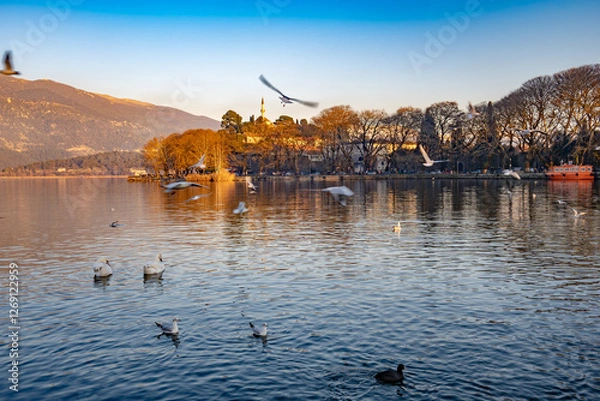 Fototapeta Ioannina lake in Epirus, Greece. Calm and reflective waters. A flock of birds is flying over the lake, adding to the peaceful atmosphere.
