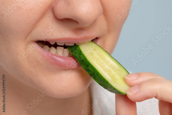 Fototapeta A close-up of a woman biting a cucumber slice, showcasing fresh and healthy eating.