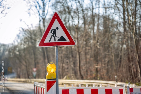 Fototapeta Road construction warning sign with illuminated safety light, work zone hazard alert, red and white striped barricade for traffic control and pedestrian safety
