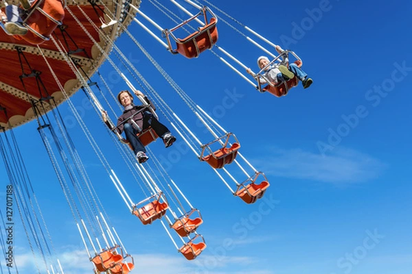 Fototapeta Mother with the six-year-old son ride an attraction on a swing agains the blue sky in amusement park