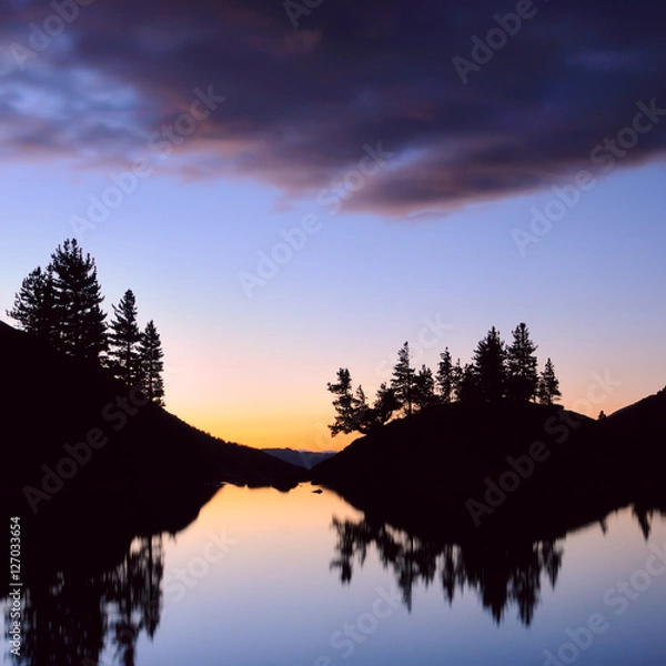 Obraz Twilight. Mountain slopes and larch trees silhouette is reflected in the smooth surface of the lake Kuyguk. Clouds backlit by the sunset, Altai