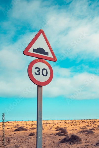 Obraz Close up shot of a 3white ad red 0 km per hour and speed bump warning against clear blue sky and deserted area behind.