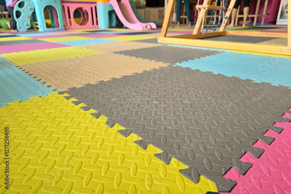Fototapeta Colorful foam play mats with textured surface in an indoor children's play area, featuring playground equipment and safety flooring.