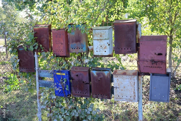 Fototapeta A bunch of old rusty mailboxes on a fence