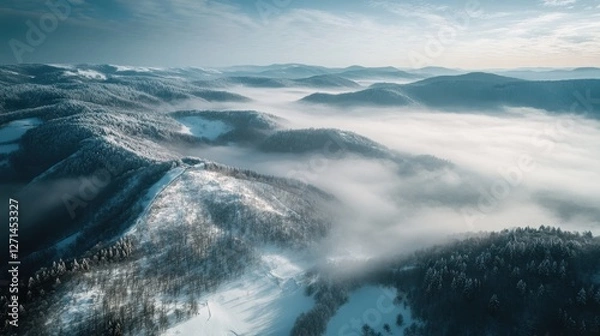 Fototapeta Aerial view of snow-covered mountain range with fog in valleys under a cloudy sky