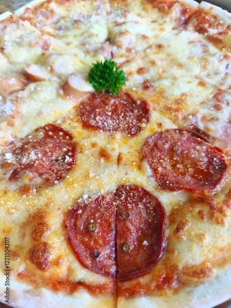 Obraz Thin and crispy pizza, divided in half, topped with pepperoni and sausage and cheese, Italian style, eight slices, placed on a wooden tray.