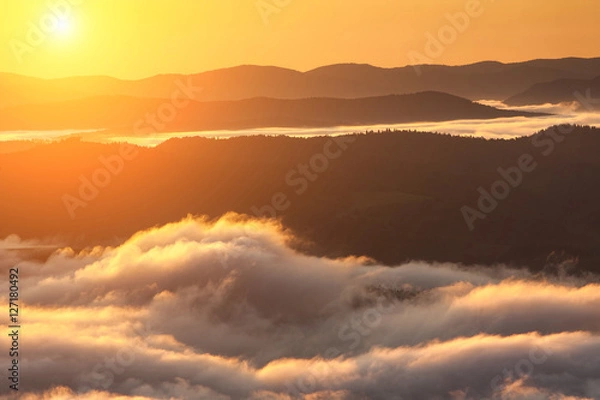 Fototapeta Summer weather phenomenon. Seasonal landscape with morning fog in valley. Clouds drenched valley below the level of the mountains. Sunrise over creeping clouds.