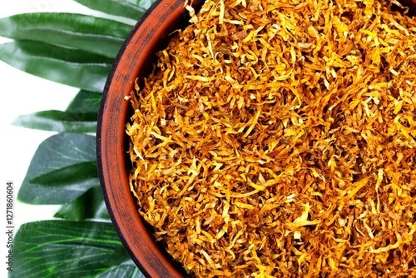 Fototapeta Fermented yellow tobacco in a brown plate on a white background with green leaves