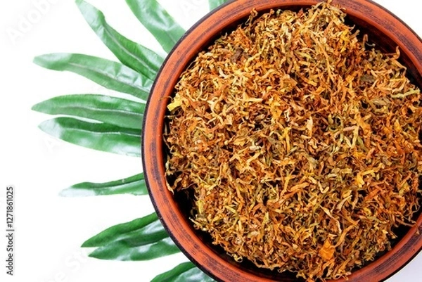 Fototapeta Fermented yellow tobacco in a brown plate on a white background with green leaves