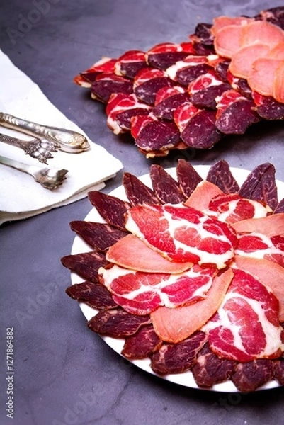 Fototapeta Sliced meat on a plate, knife and tongs on a white napkin, on a gray background