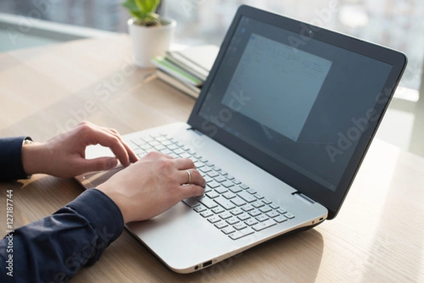 Fototapeta Hands typing on a laptop keyboard. A man works in an office at his workplace