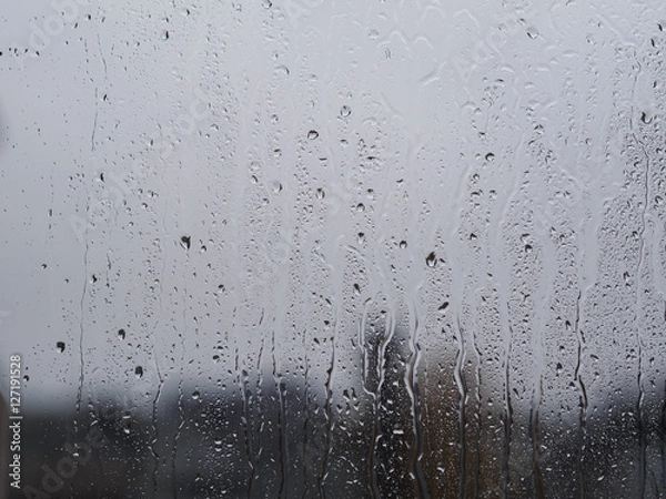 Fototapeta Regentropfen auf Fensterscheibe mit Gebäuden im Hintergrund