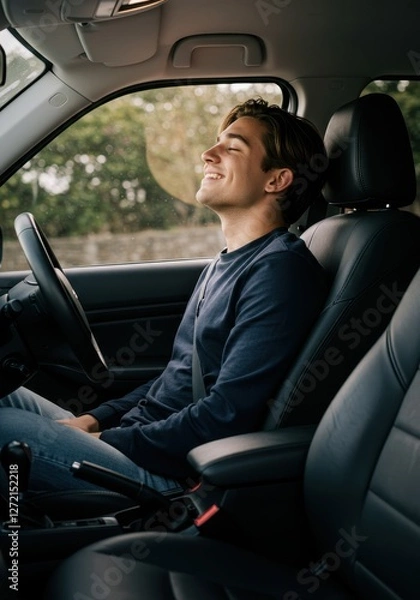 Fototapeta A young man relaxes in a parked car, smiling and enjoying the calm outdoors on a sunny day