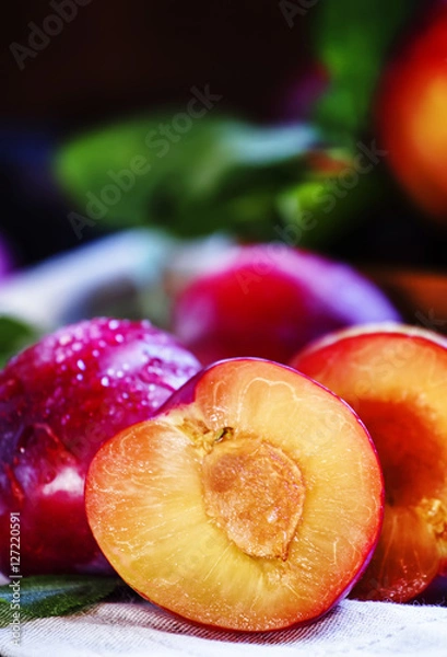 Fototapeta Red plums, cut in half, vintage wooden background, rustic style,