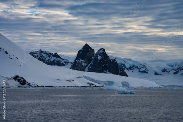 Fototapeta Antarctic Peninsula: Snowy peaks, icebergs, cloudy sky. Lemaire Channel