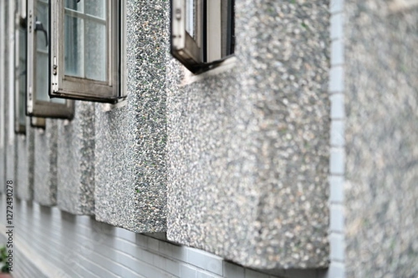 Fototapeta A textured terrazzo-framed window set on a clean white brick wall, highlighting a blend of Japanese and modern minimalist design. The uniform row of glass windows enhances the structural harmony.
