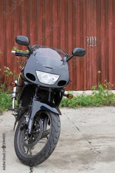 Fototapeta Black motorcycle parked in front of a wooden fence on a concrete surface