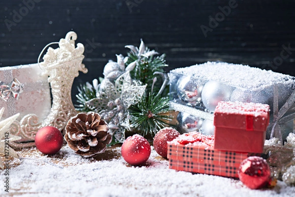 Fototapeta Holidays background. Toys and presents on a dark wooden background with a lot of snow. Pine cones, presents, Christmas balls and other toys on a snow background.