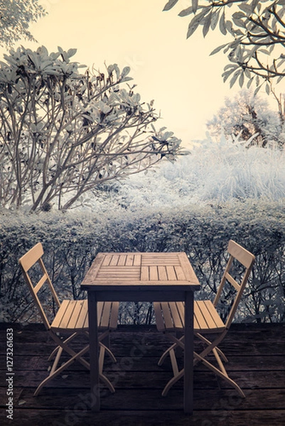 Fototapeta Infrared photography, a serene outdoor setting featuring a small wooden table and two chairs positioned in front of a lush green hedge