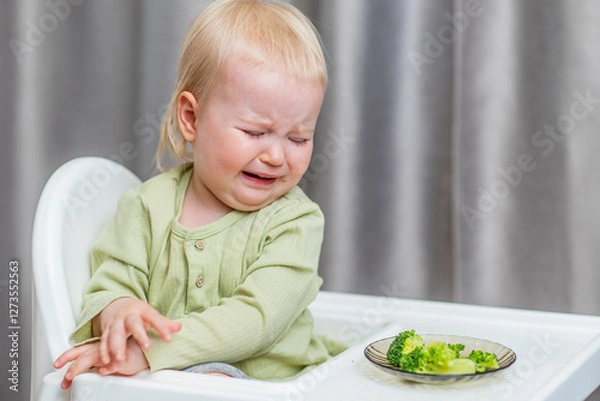 Obraz Cute baby refuses to eat broccoli at the kitchen table