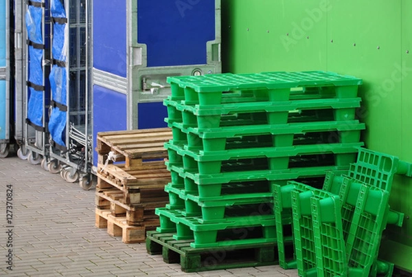 Fototapeta Store unloading. Green Plastic and wooden pallets for storage of containers.