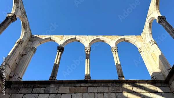 Fototapeta Arched ruins of an ancient structure against a clear blue sky. The stone columns with intricately carved capitals evoke a sense of antiquity and history
