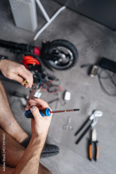 Fototapeta man tries to fix an electric scooter with his own hands at home. Electricity and the danger of getting an electric shock.