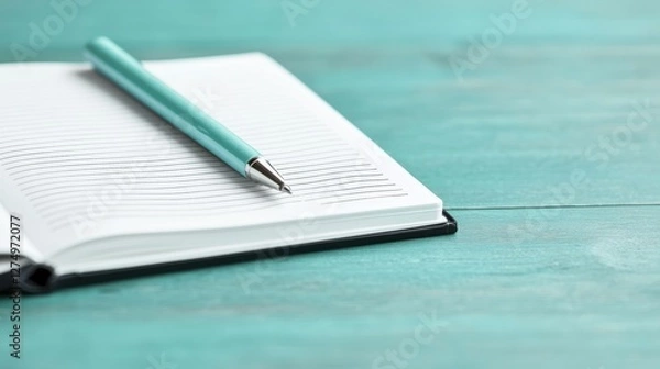 Fototapeta Writing in a notebook with a pen on a teal wooden surface close-up photography minimalist aesthetic calm environment creative concept
