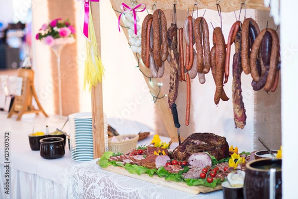 Obraz Jedzenie w formie bufetu, stół wiejski, stół szwedzki. Posiłki, wyrzywienie dla ludzi podczas zabawy, imprezy weselnej: mięso, ser, pasztet, kiełbasa, smalec, szynka, przyprawy, sałata, pierogi, wódka