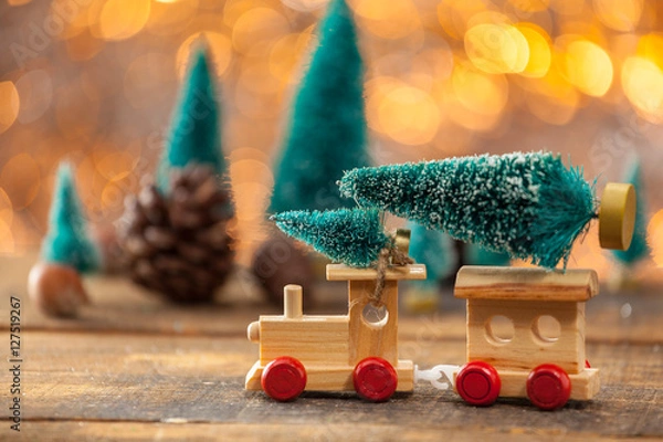Obraz Miniature Toy Train Towing A Christmas Tree On A Wooden Backgrou