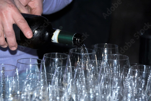 Fototapeta sommelier pouring white wine in rows of empty glasses