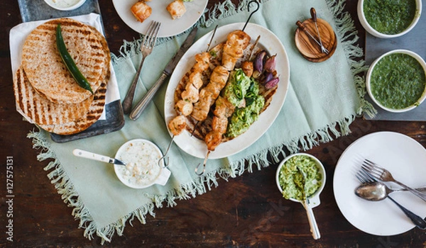 Fototapeta Mexican food table with chicken skewers, avocado cream sauce, and flatbread. 
