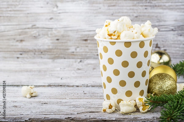 Fototapeta Salty fresh crusty homemade popcorn in silver paper cup in the fashion light background of white brick wall in a New Year's interior with Christmas balls. selective focus