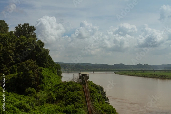 Fototapeta Military Watchtower Overlooking Calm River And Green Landscape With Bridges And Rolling Hills Under Cloudy Sky