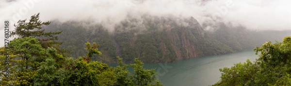 Fototapeta Steep Mist-Covered Mountain Cliffs Overlooking a Serene Emerald Lake Surrounded by Dense Greenery in Taiwan