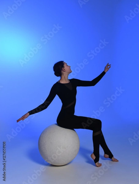 Obraz young girl dancer sitting on a ball. Dancer in a black jumpsuit